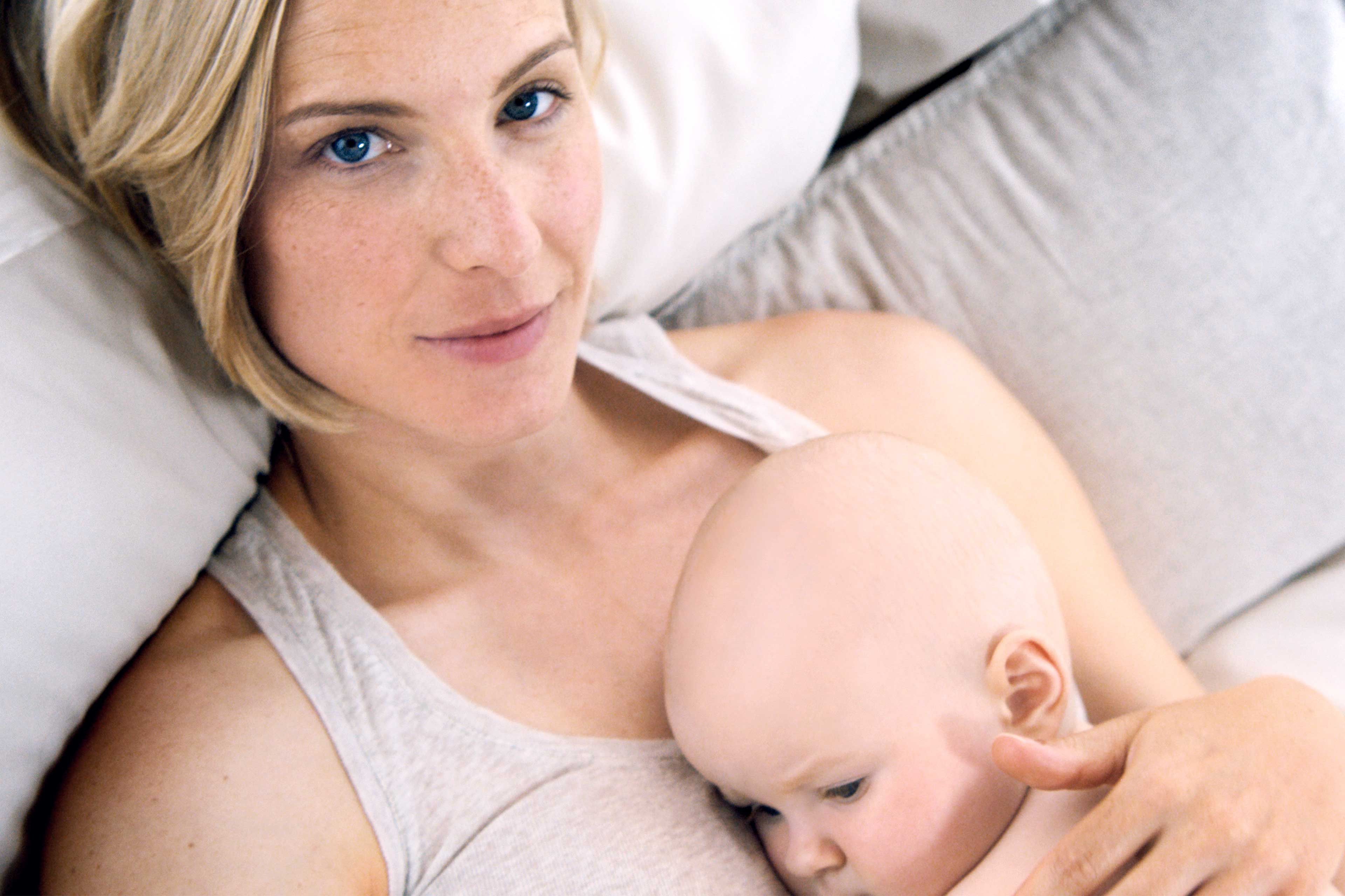 Frau liegt auf einem Kissen und hält ein Baby im Arm