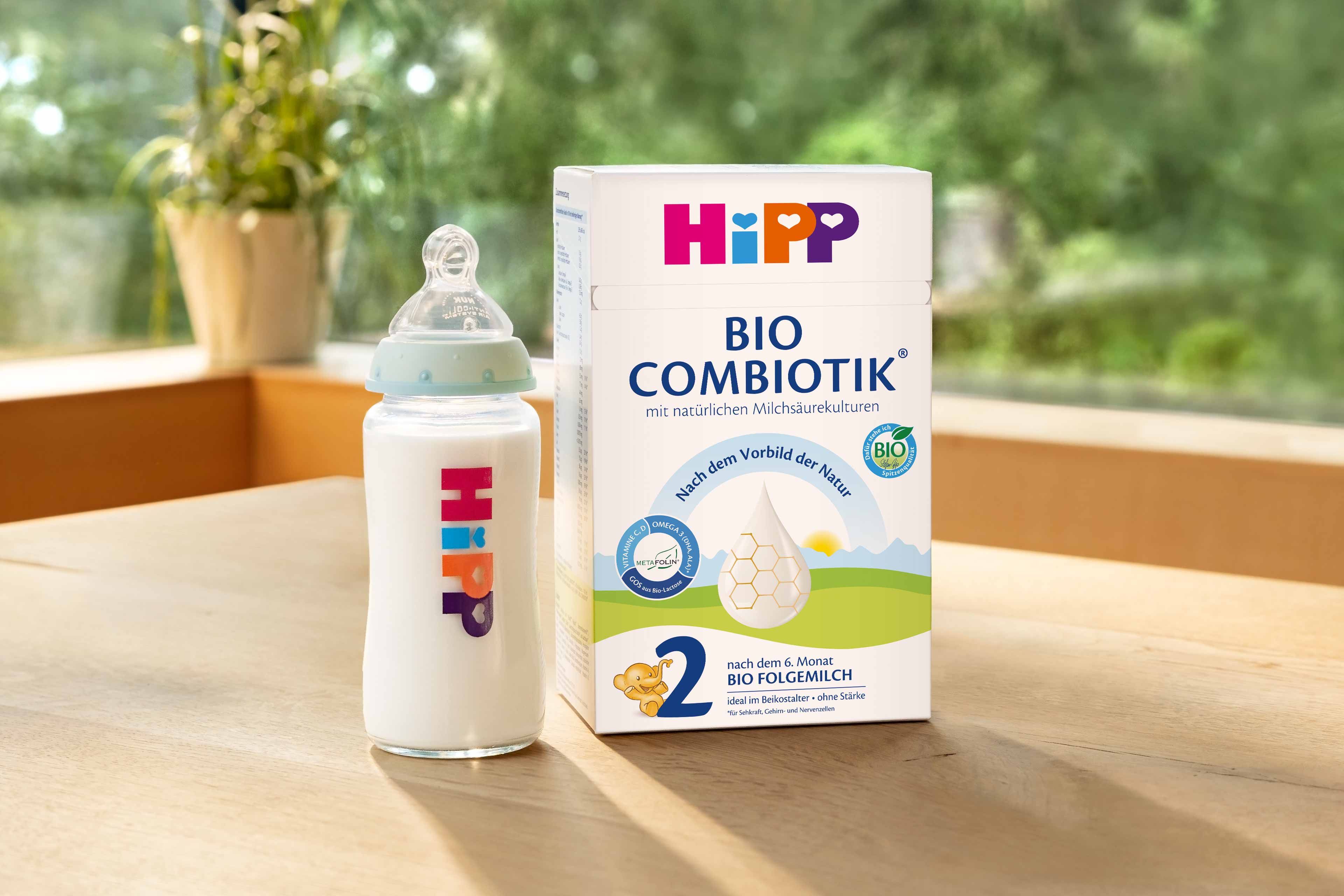 HiPP 2 BIO COMBIOTIK Folgemilch-Packung mit gefüllter Babyflasche auf Holztisch, daneben blauer Kreis mit „Jetzt kostenlos testen!“