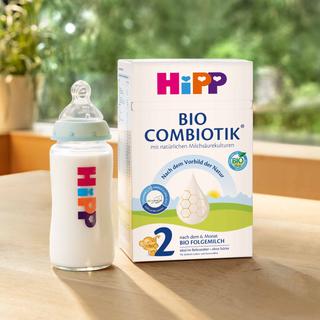 HiPP 2 BIO COMBIOTIK Folgemilch-Packung mit gefüllter Babyflasche auf Holztisch, daneben blauer Kreis mit „Jetzt kostenlos testen!“