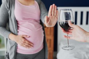 Eine Frau in einem rosa Oberteil und einer grauen Strickjacke lehnt ein Glas Wein mit der Hand ab.