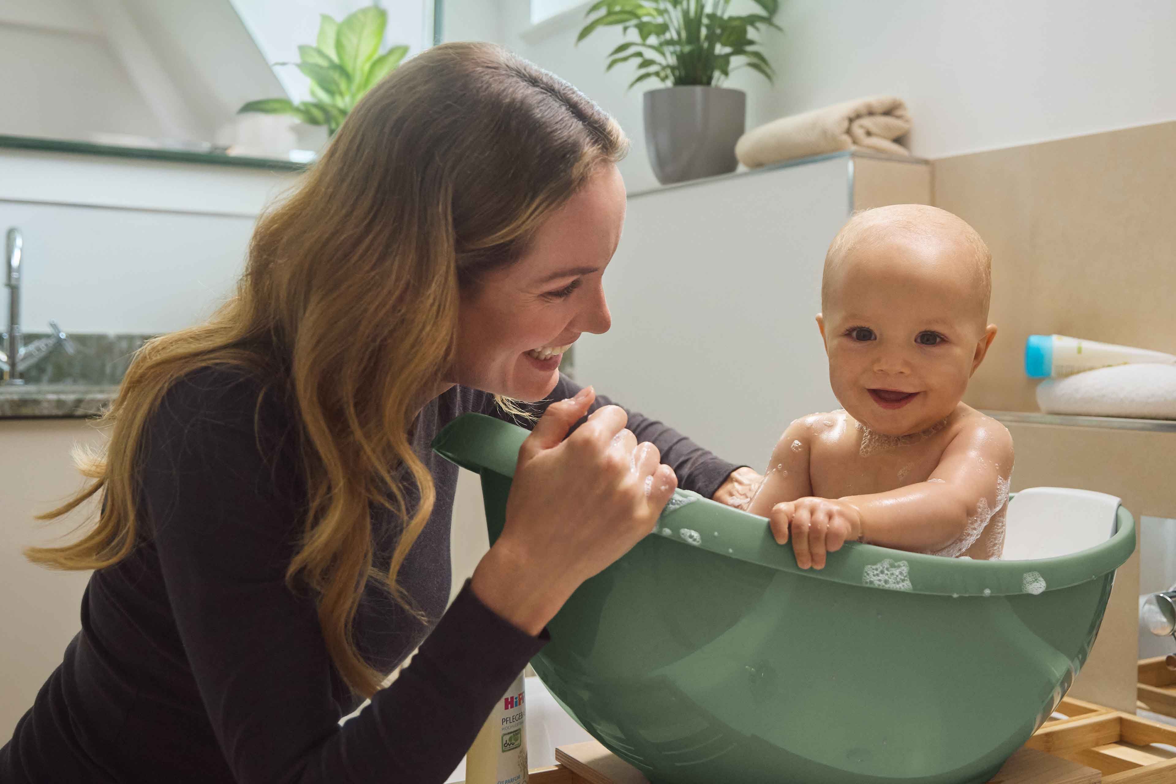 Eine Frau badet ein Baby in einer grünen Schüssel.