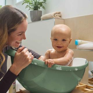 Eine Frau badet ein Baby in einer grünen Schüssel.