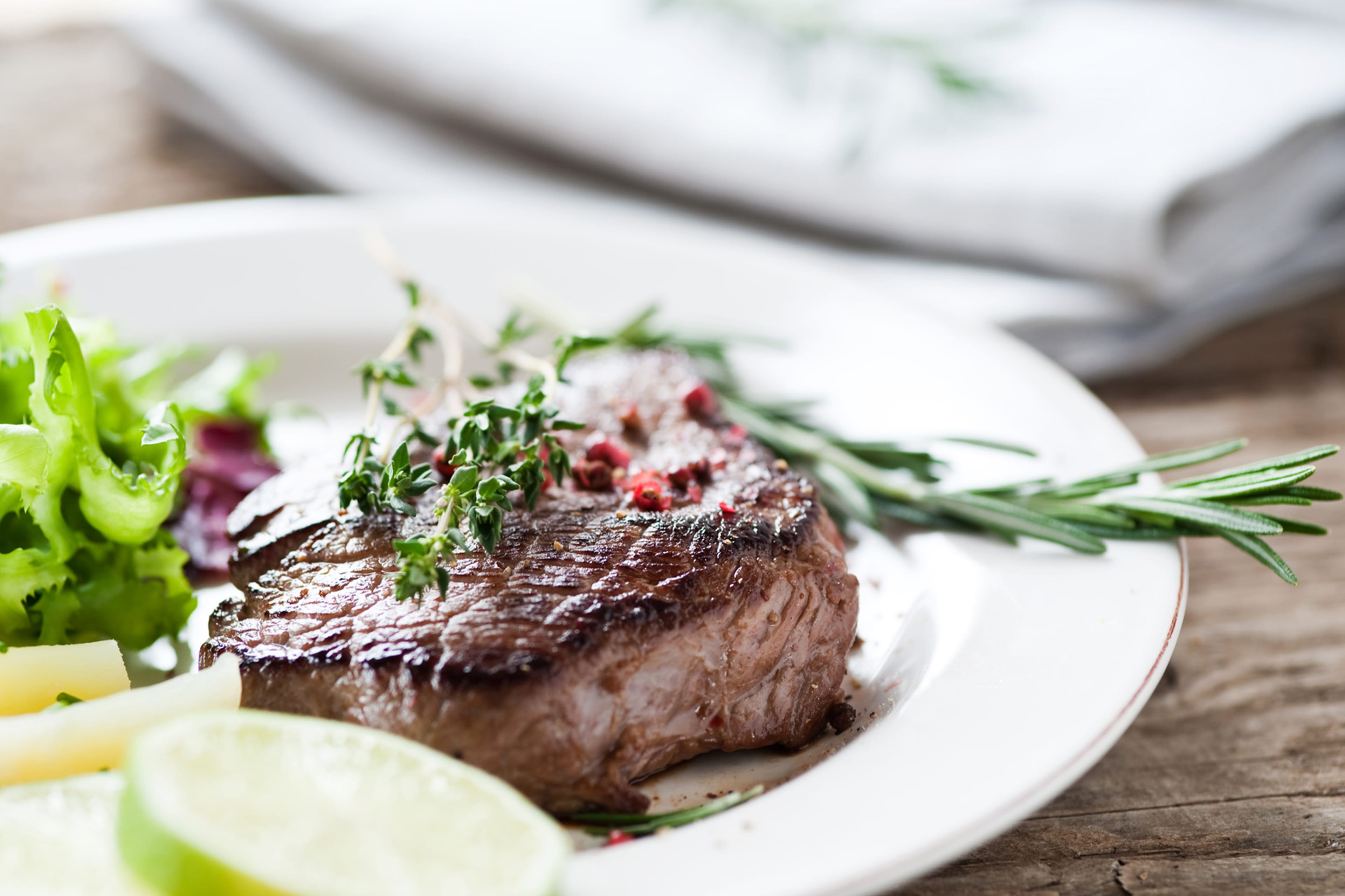 Ein gegrilltes Stück Fleisch, garniert mit Kräutern und einer Limettenscheibe, begleitet von einer Beilage aus grünem Gemüse.