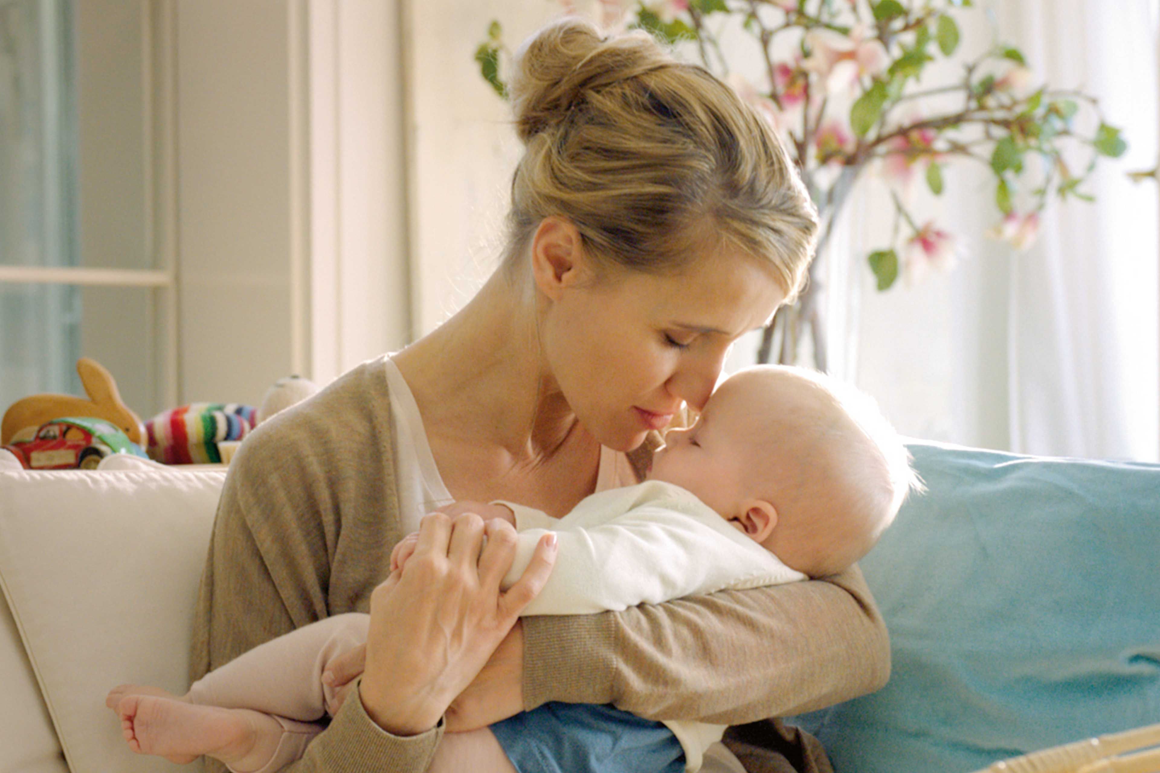 Ein zärtlicher Moment zwischen einer Mutter und ihrem Baby, in dem die Mutter sanft die Stirn des Babys küsst.