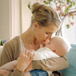 Ein zärtlicher Moment zwischen einer Mutter und ihrem Baby, in dem die Mutter sanft die Stirn des Babys küsst.