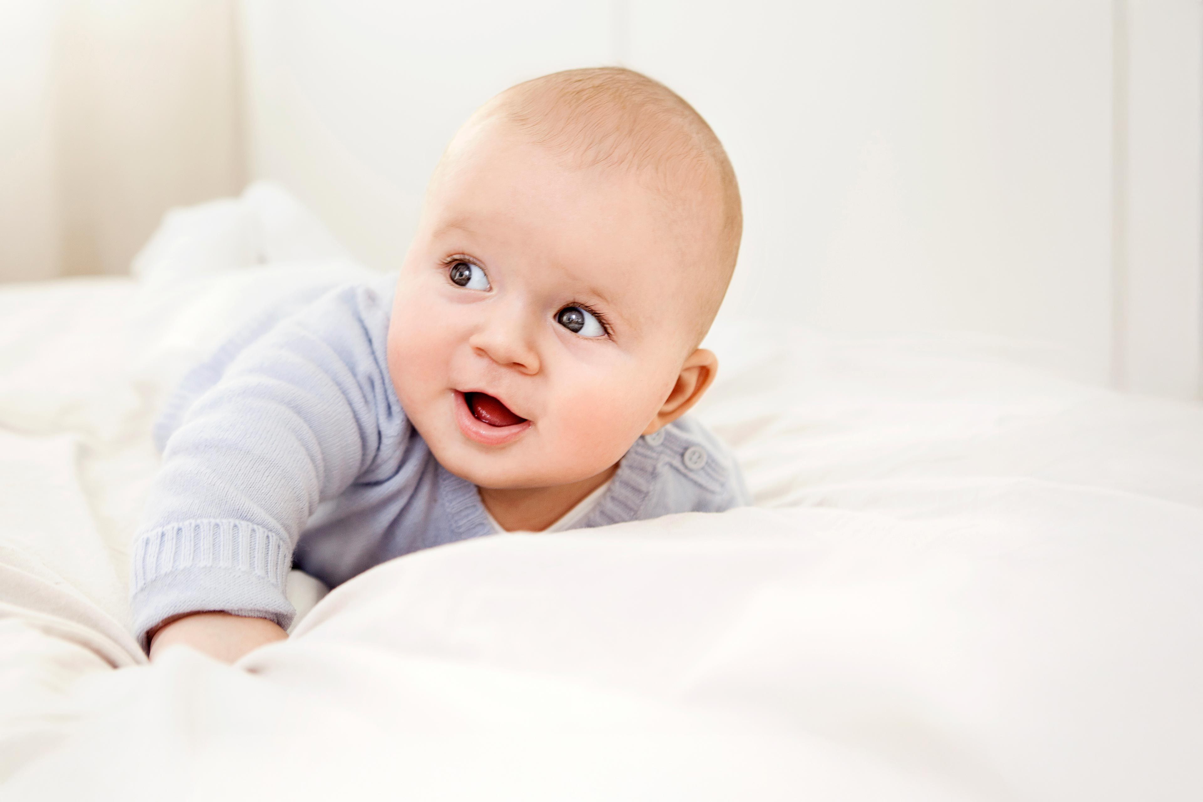 Baby liegt auf dem Bauch auf weißer Bettdecke in hellem Raum