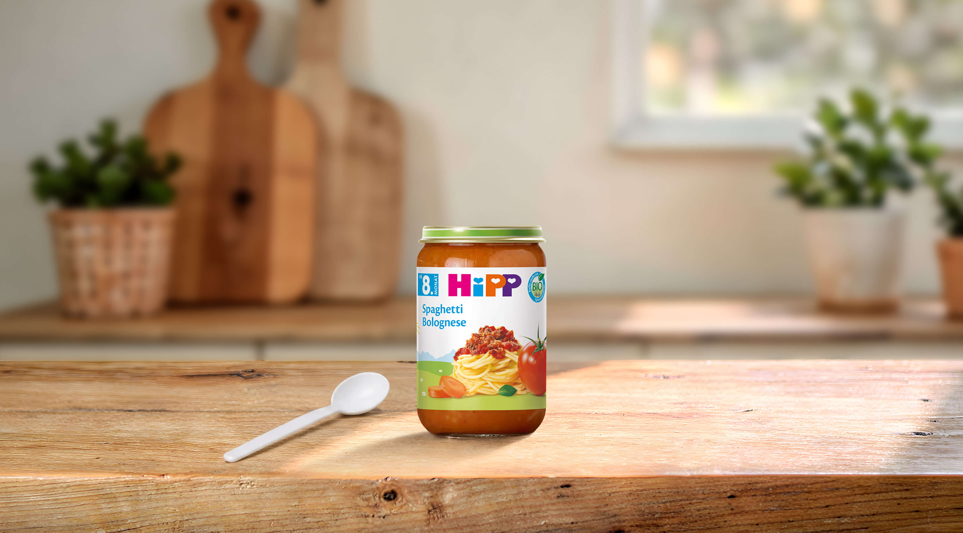 HiPP Bio Babyglas Spaghetti Bolognese 220g auf Holztisch mit Löffel in heller, gemütlicher Küchenumgebung