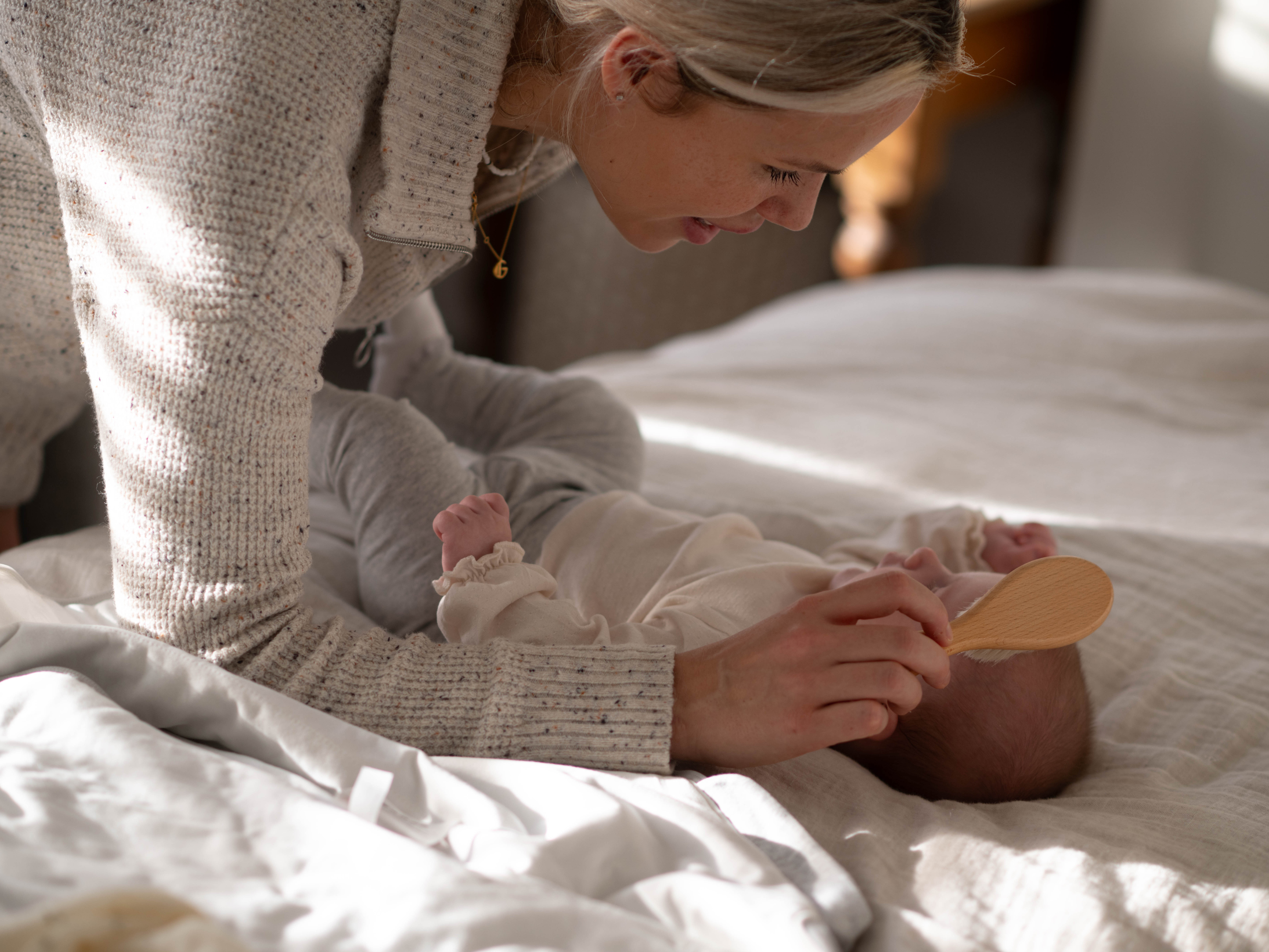 Smiling parent gently brushing their baby’s hair on a cosy bed in soft natural light