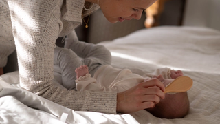Smiling parent gently brushing their baby’s hair on a cosy bed in soft natural light