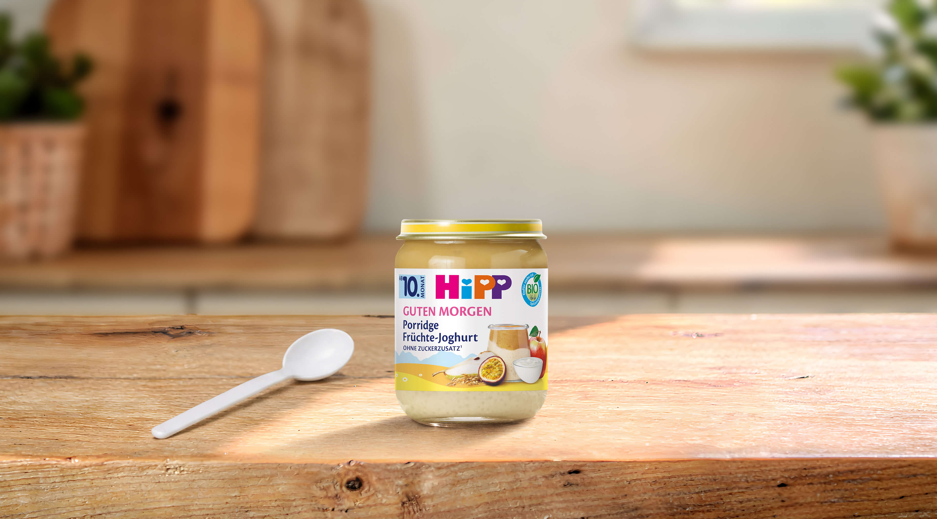 HiPP Guten Morgen Porridge Früchte-Joghurt Bio-Babybrei im Glas auf Holztisch mit Löffel in heller Küchenumgebung