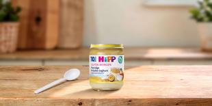 HiPP Guten Morgen Porridge Früchte-Joghurt Bio-Babybrei im Glas auf Holztisch mit Löffel in heller Küchenumgebung