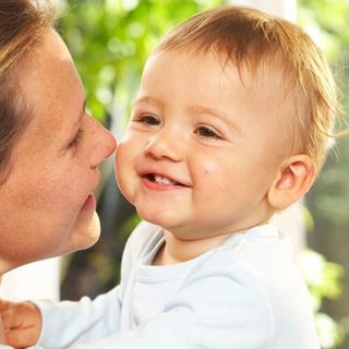 Lächelndes Baby im Arm eines Elternteils, innige Nähe und Geborgenheit beim Stillen und Füttern mit Muttermilch