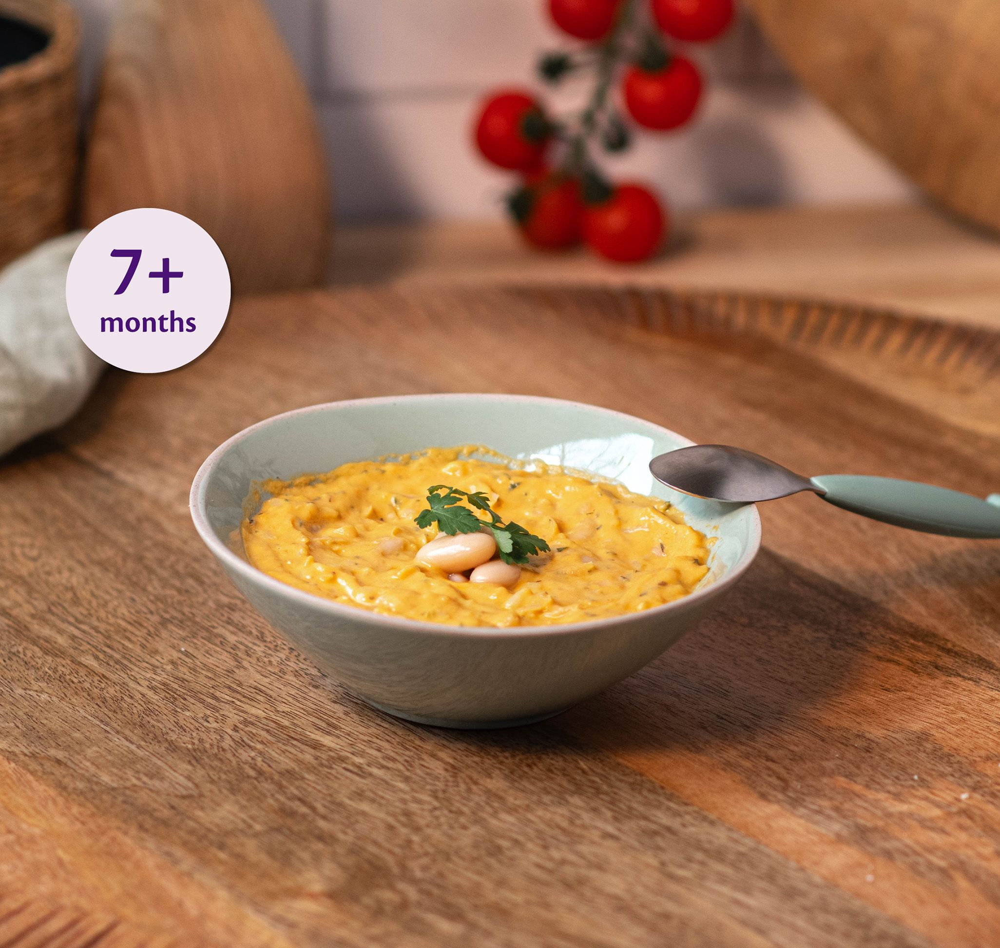 Bowl of cheesy veggie bean mash for babies 7+ months on a wooden table with a baby spoon beside it