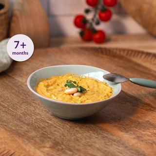Bowl of cheesy veggie bean mash for babies 7+ months on a wooden table with a baby spoon beside it
