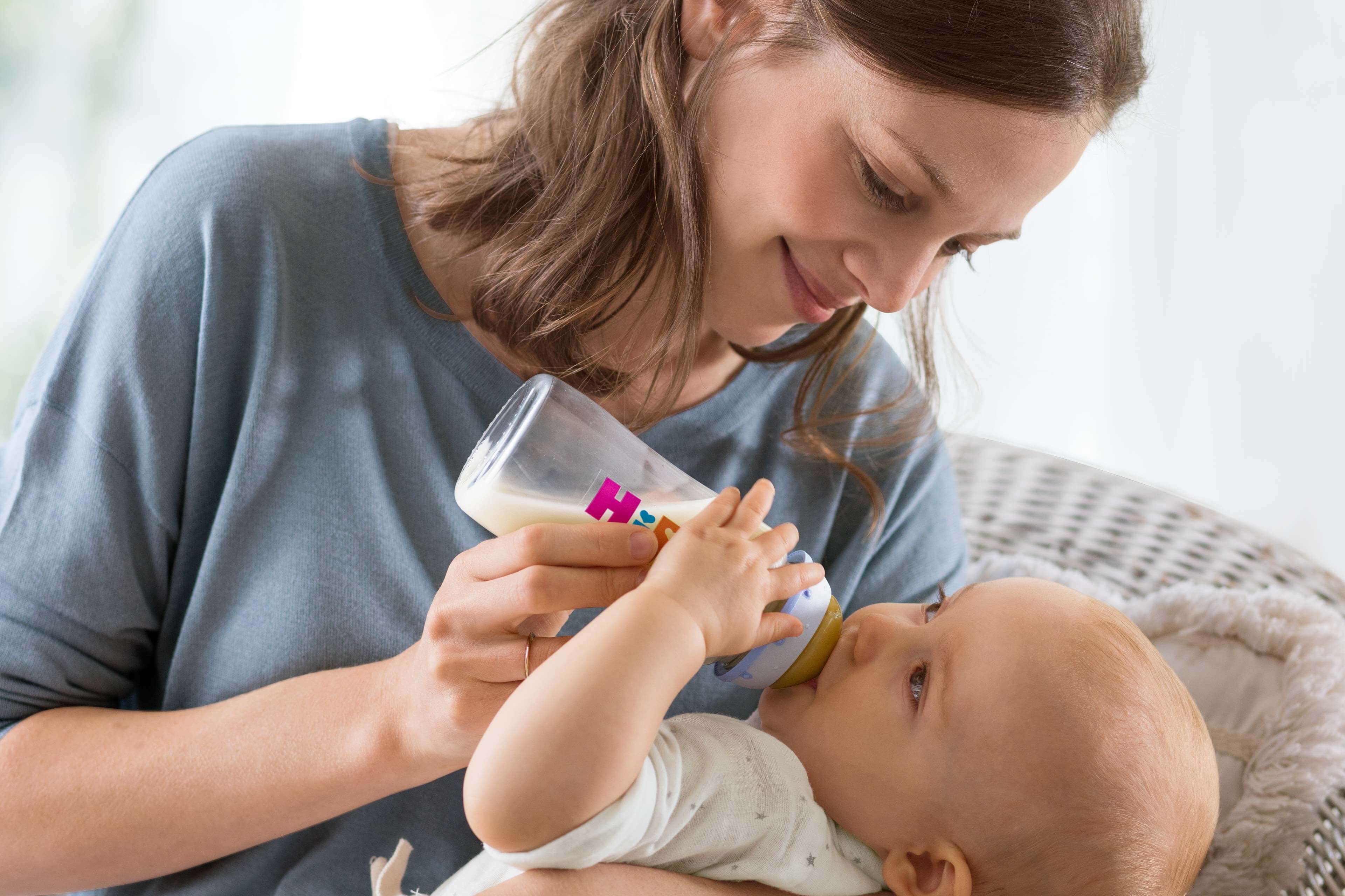 Mutter füttert ihr Baby liebevoll mit einem Fläschchen Milchnahrung im Arm sitzend