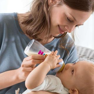 Mutter füttert ihr Baby liebevoll mit einem Fläschchen Milchnahrung im Arm sitzend