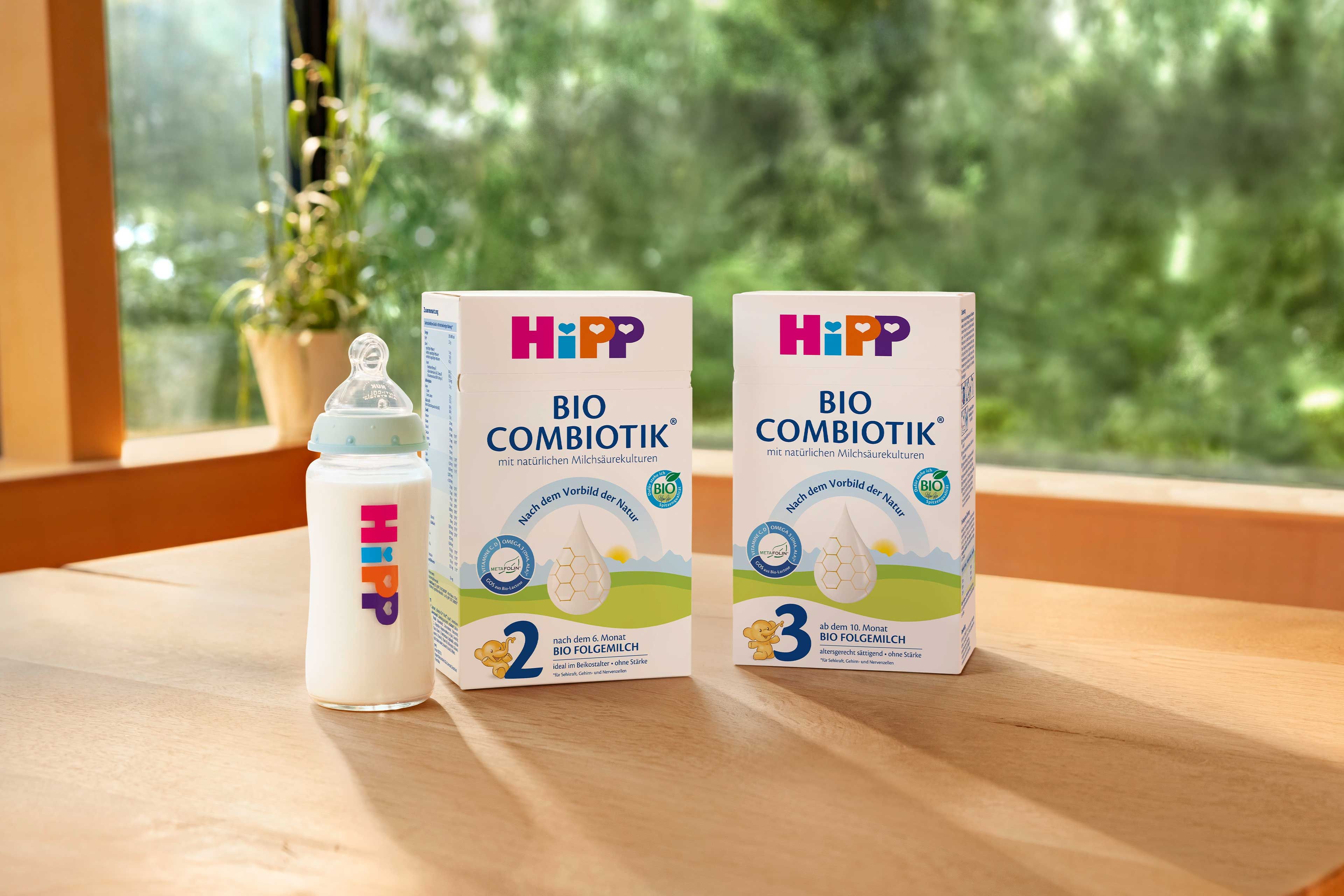 HiPP Babyflasche neben Packungen BIO COMBIOTIK® 2 und 3 auf einem Holztisch