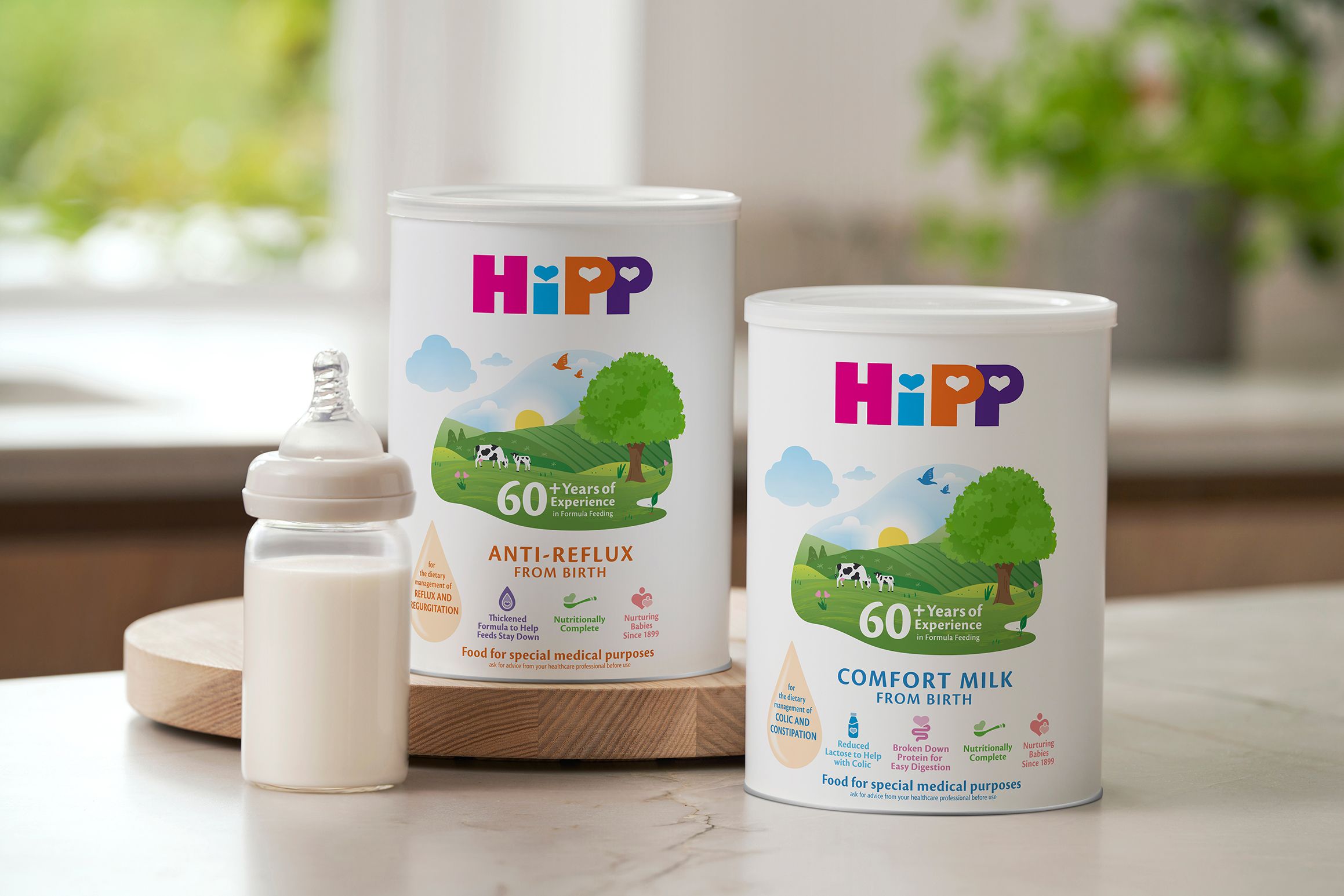 HiPP Organic Anti-Reflux and Comfort Milk tins on a kitchen worktop beside a prepared baby bottle of formula
