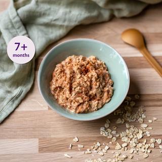 Bowl of overnight oats with grated carrot and apple on a wooden surface, with oats scattered and a label reading 7+ months