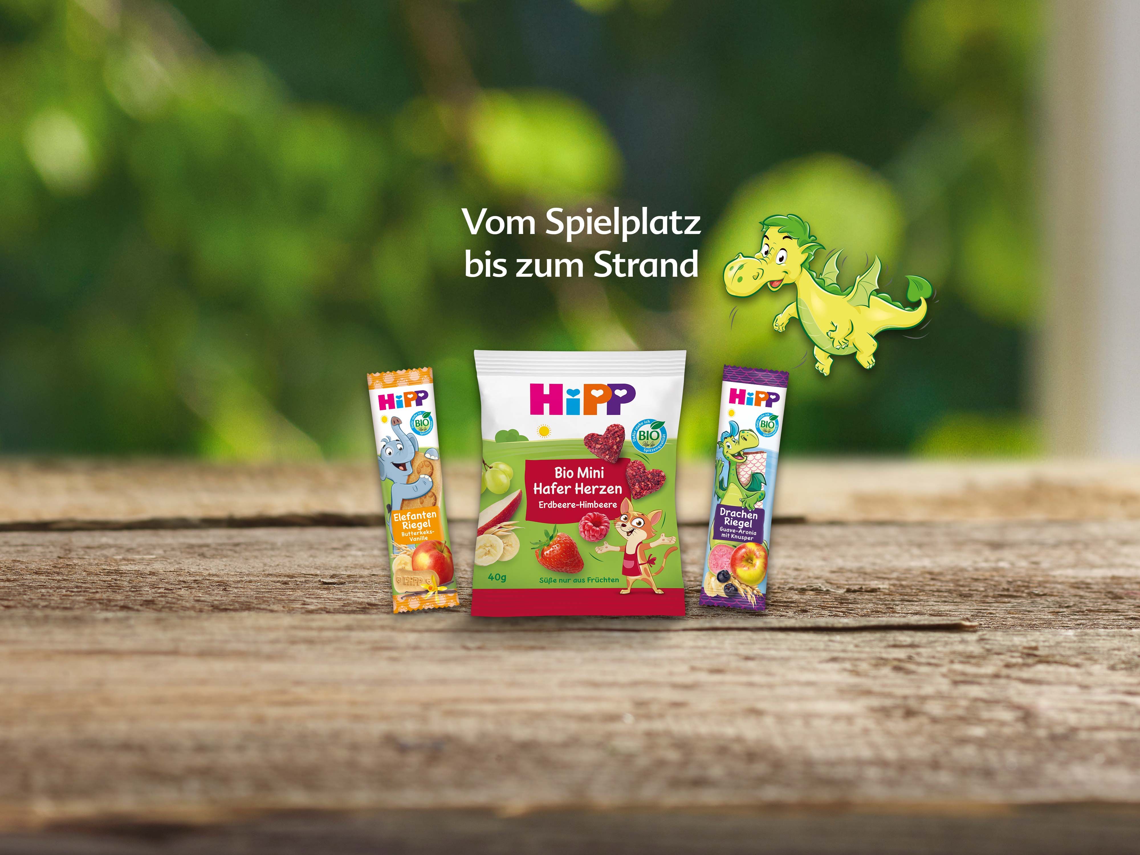 Drei Hipp-Produkte für Kinder mit der Aufschrift 'Vom Spielplatz bis zum Strand' und einer grünen Dinosaurierillustration