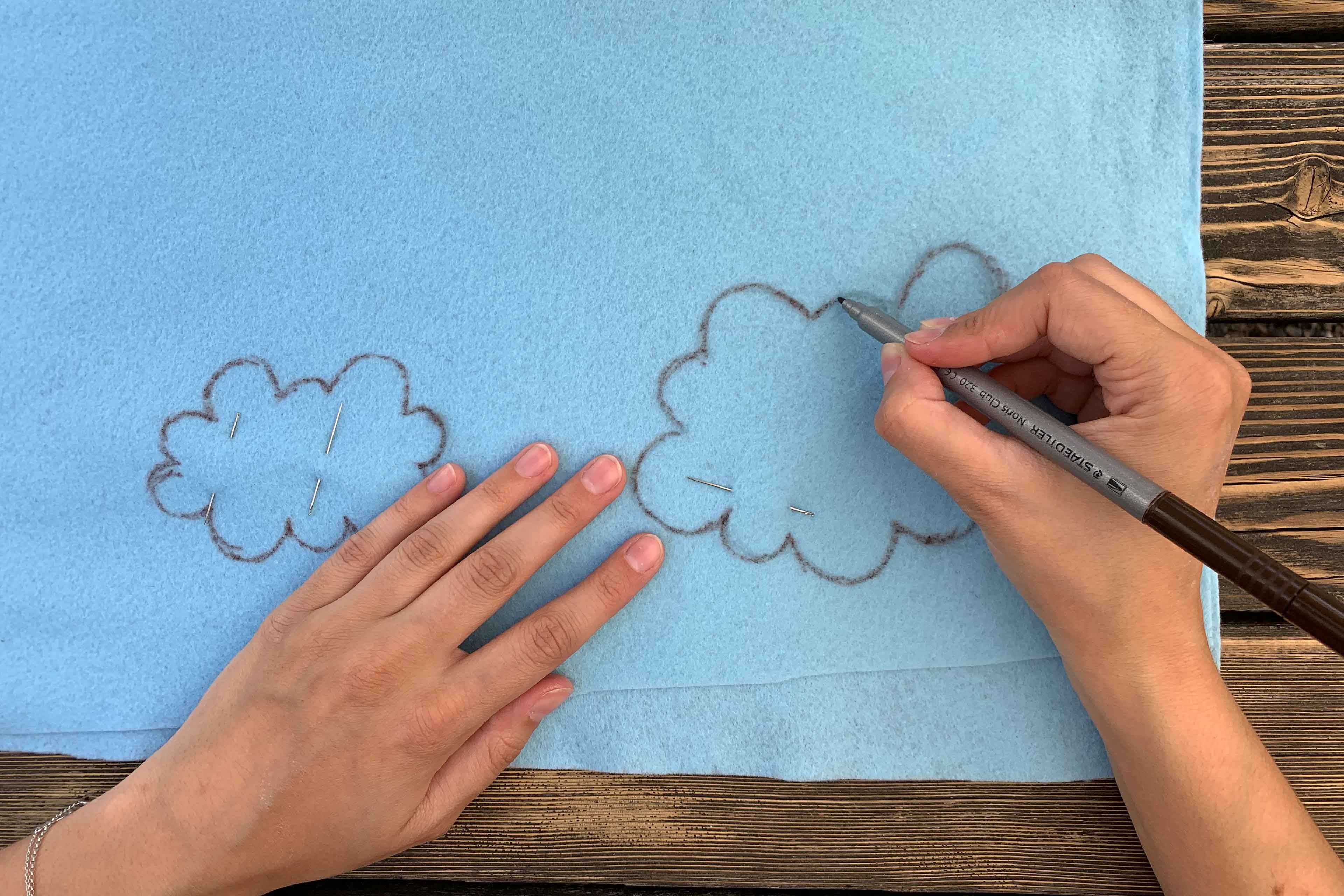 Eine Hand zeichnet zwei wolkenähnliche Formen auf einen blauen Stoff.