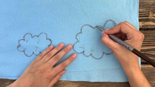 Eine Hand zeichnet zwei wolkenähnliche Formen auf einen blauen Stoff.