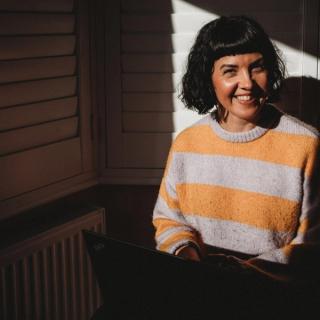 Photo of Lucy Wood, Paediatric Dietitian smiling, sitting by a window with a laptop