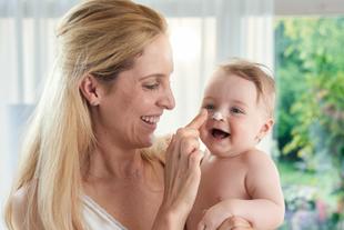 Lachende Mutter hält ihr Baby im Arm und tupft ihm spielerisch Creme auf die Nase