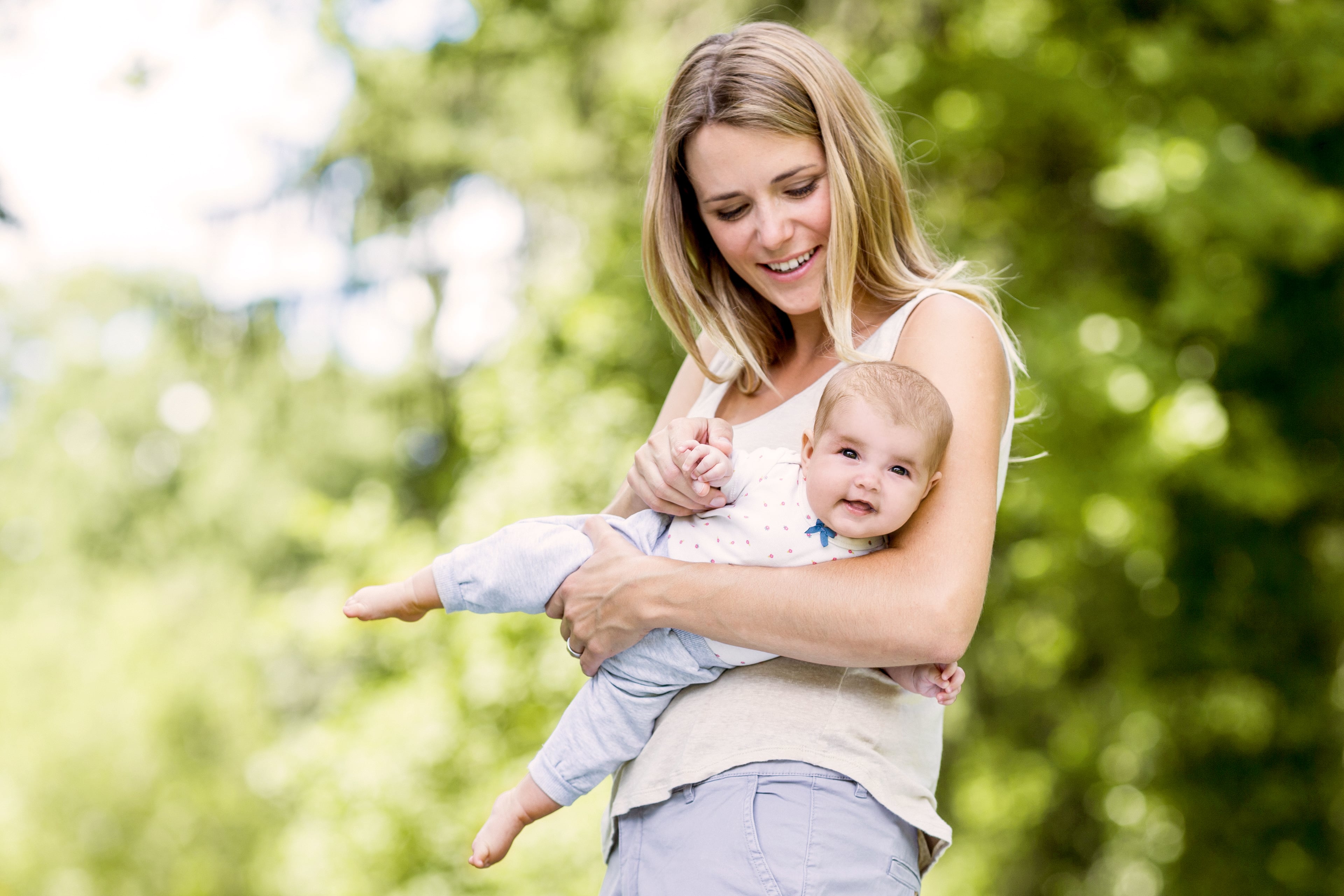 Eine Frau hält ein Baby im Freien mit Grünzeug im Hintergrund.