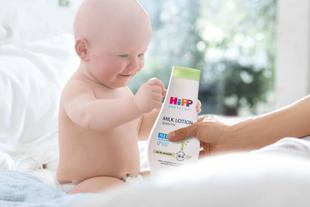 Ein scheinbar gut gelauntes Baby hält ein Fläschchen mit der Aufschrift "HIP BABY SENSITIVE" und der Aufschrift "Milk Lotion".
