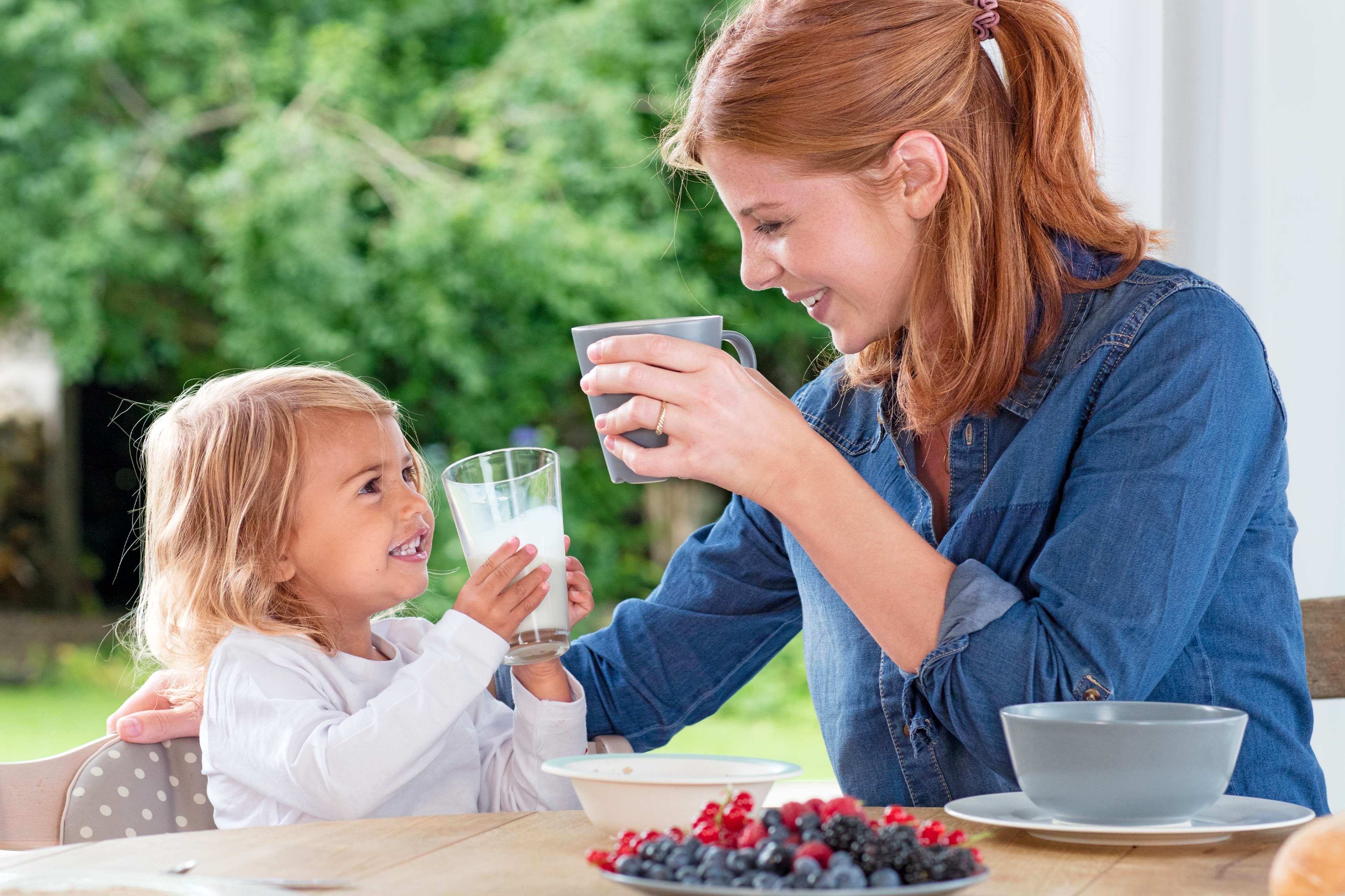 Ein fröhlicher Moment zwischen einer Mutter und ihrer kleinen Tochter, die im Freien ein Glas Milch trinken.