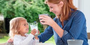 Ein fröhlicher Moment zwischen einer Mutter und ihrer kleinen Tochter, die im Freien ein Glas Milch trinken.