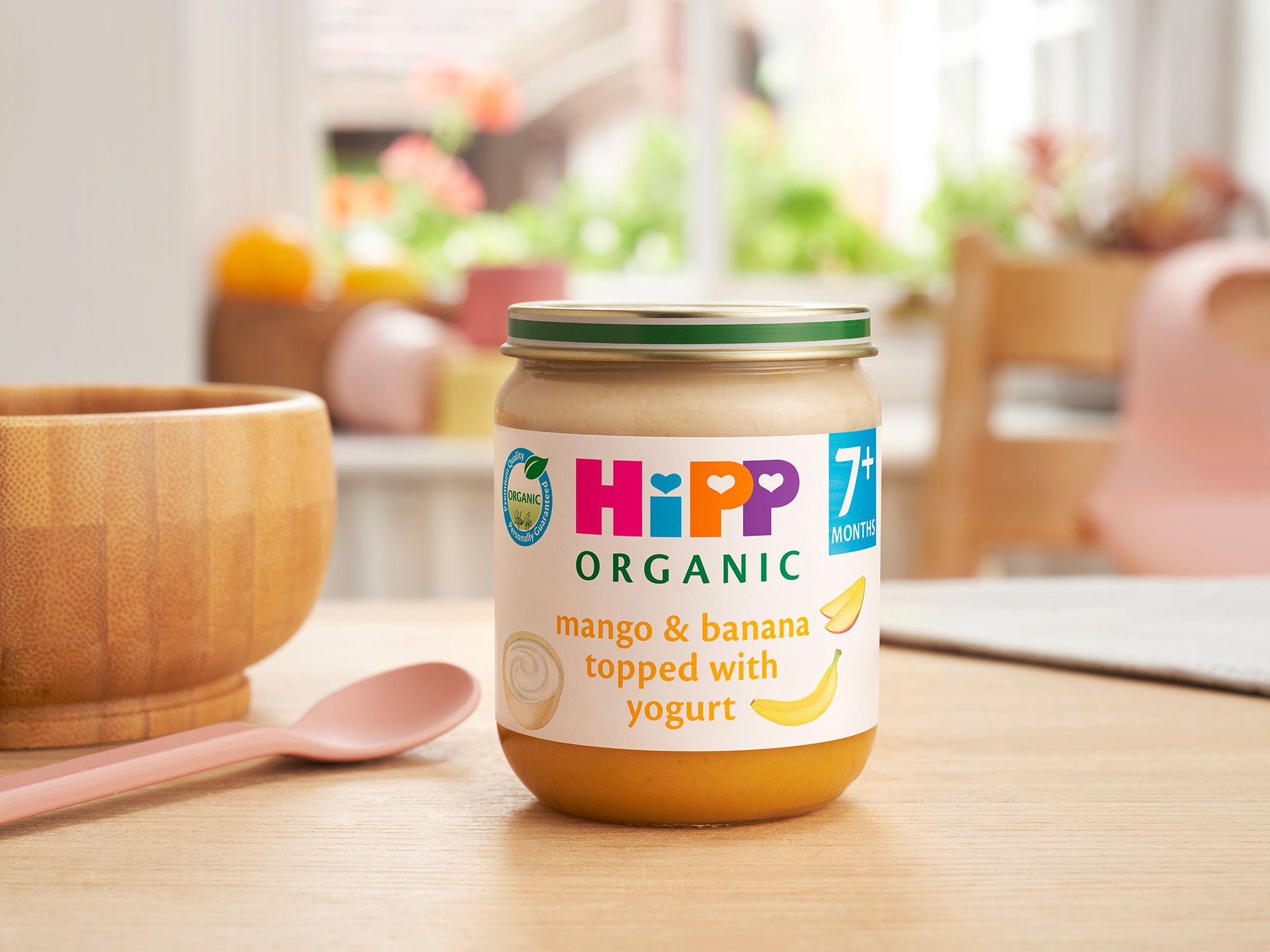 HiPP Organic Mango & Banana topped with Yogurt on a dining table next to a bowl and spoon