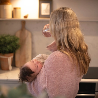 Mum holding sleeping baby whilst drinking some water