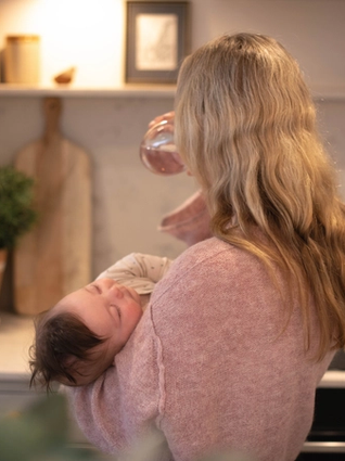Mum holding sleeping baby whilst drinking some water
