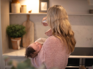Mum holding sleeping baby whilst drinking some water