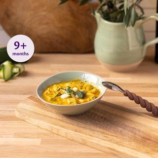 Bowl of mild fish and courgette curry for babies 9+ months on a wooden board with a baby spoon beside it