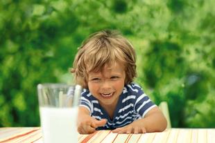 Ein fröhliches Kind, das nach einem Glas Milch greift.