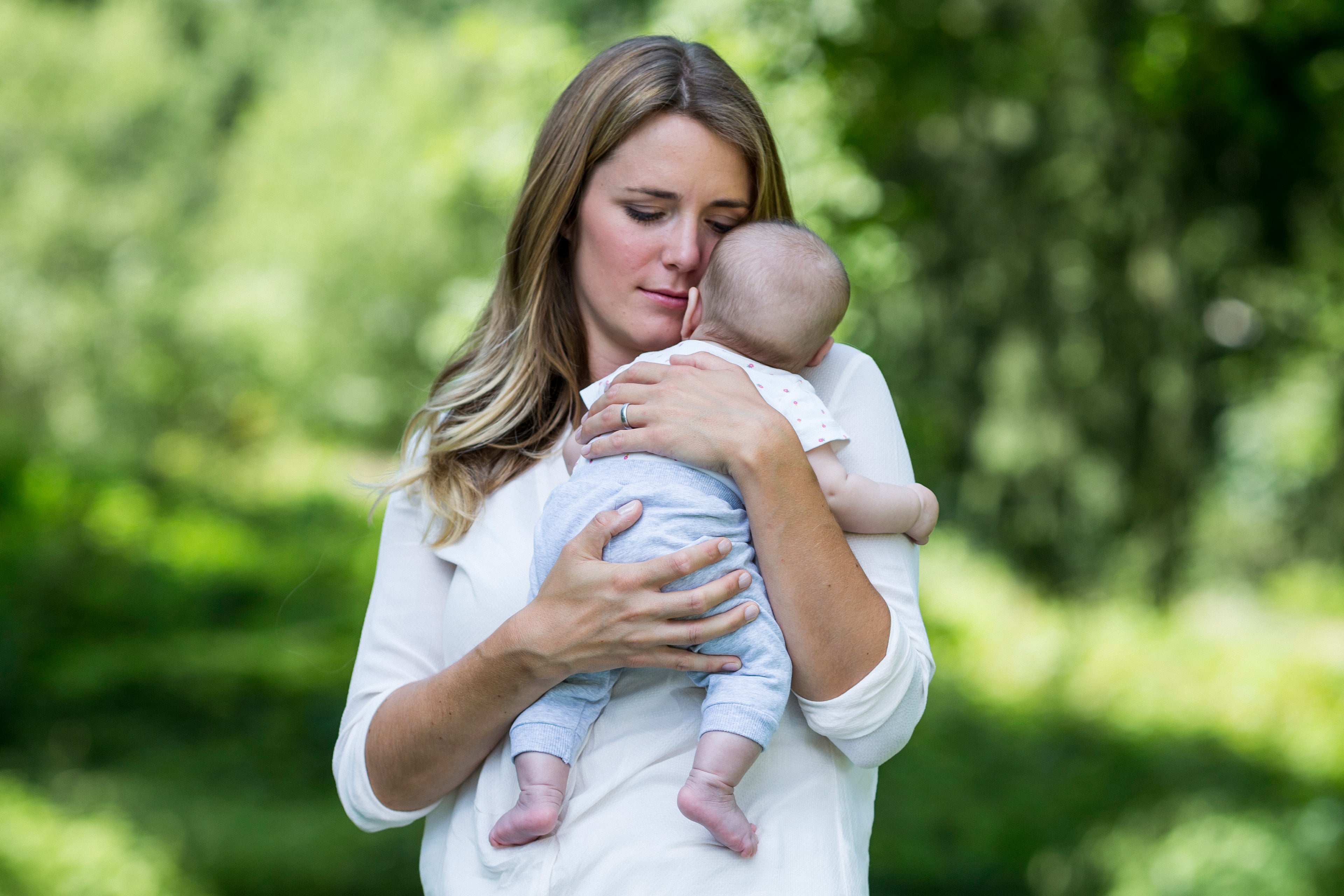 Eine Frau mit blondem Haar, die ein Baby an ihr Gesicht drückt, beide scheinen in einem ruhigen Moment zu sein.
