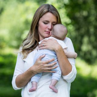 Eine Frau mit blondem Haar, die ein Baby an ihr Gesicht drückt, beide scheinen in einem ruhigen Moment zu sein.