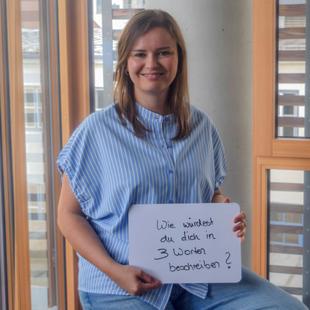 Eine HiPP Mitarbeiterin hält ein Schild mit 'Wie würdest du dich in 3 Worten beschreiben?'