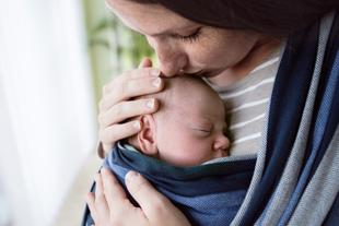 Ein zärtlicher Moment zwischen einer Mutter und ihrem neugeborenen Baby, in dem die Mutter sanft die Stirn des Babys küsst.