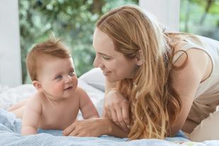 Ein zärtlicher Moment zwischen einer Mutter und ihrem Baby, wobei die Mutter sanft mit dem Kind auf einem Bettchen umgeht.