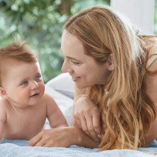 Ein zärtlicher Moment zwischen einer Mutter und ihrem Baby, in dem die Mutter sanft mit dem Baby interagiert, beide umgeben von einer ruhigen Umgebung.