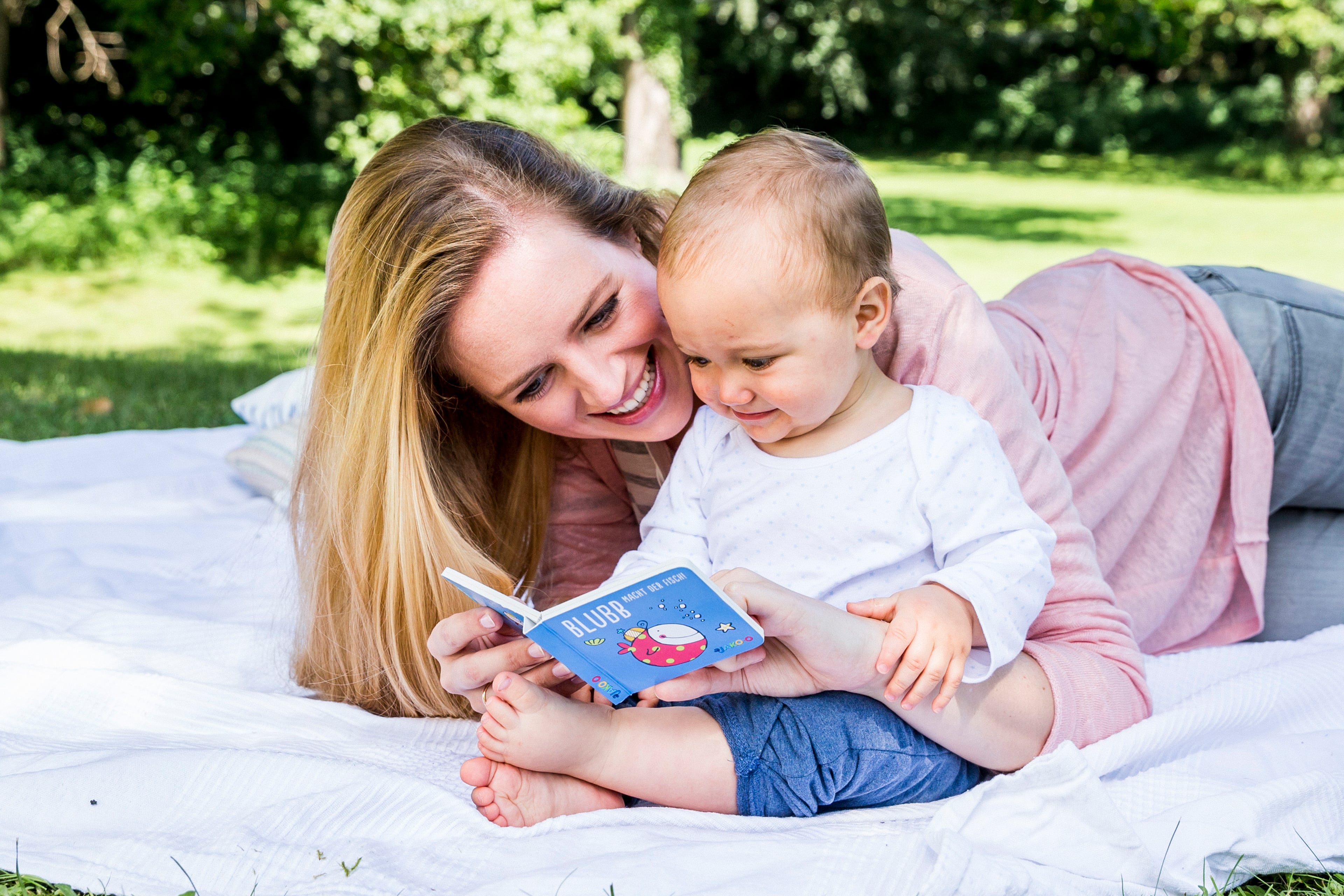 Ein freudiger Moment zwischen einer Frau und einem Baby, in dem die Frau dem Baby im Freien ein Buch vorliest.