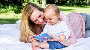 Ein freudiger Moment zwischen einer Frau und einem Baby, in dem die Frau dem Baby im Freien ein Buch vorliest.