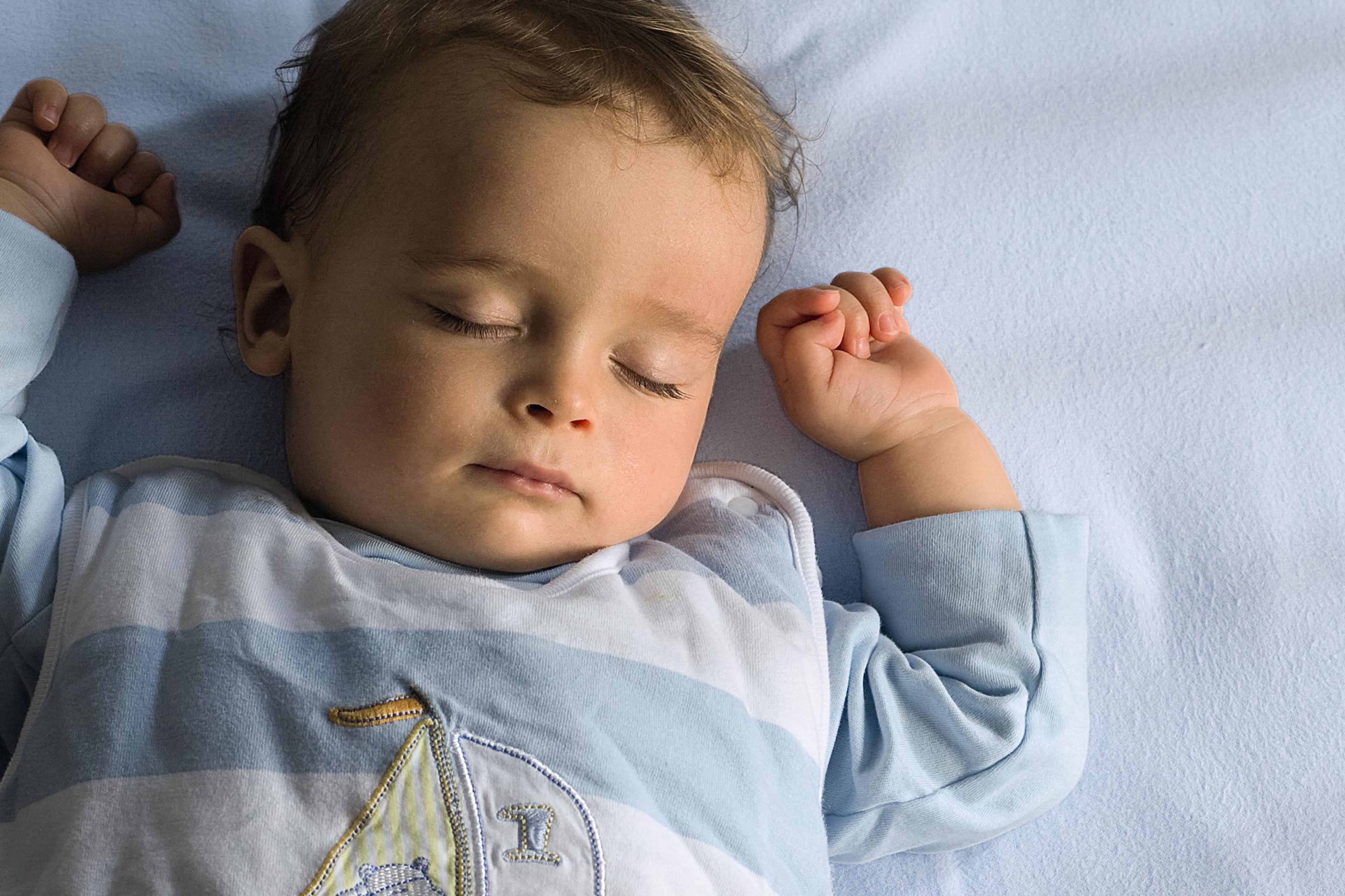 Ein scheinbar tief schlafendes Baby mit geschlossenen Augen und entspanntem Gesichtsausdruck, das auf einer blauen Fläche ruht.