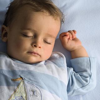 Ein scheinbar tief schlafendes Baby mit geschlossenen Augen und entspanntem Gesichtsausdruck, das auf einer blauen Fläche ruht.