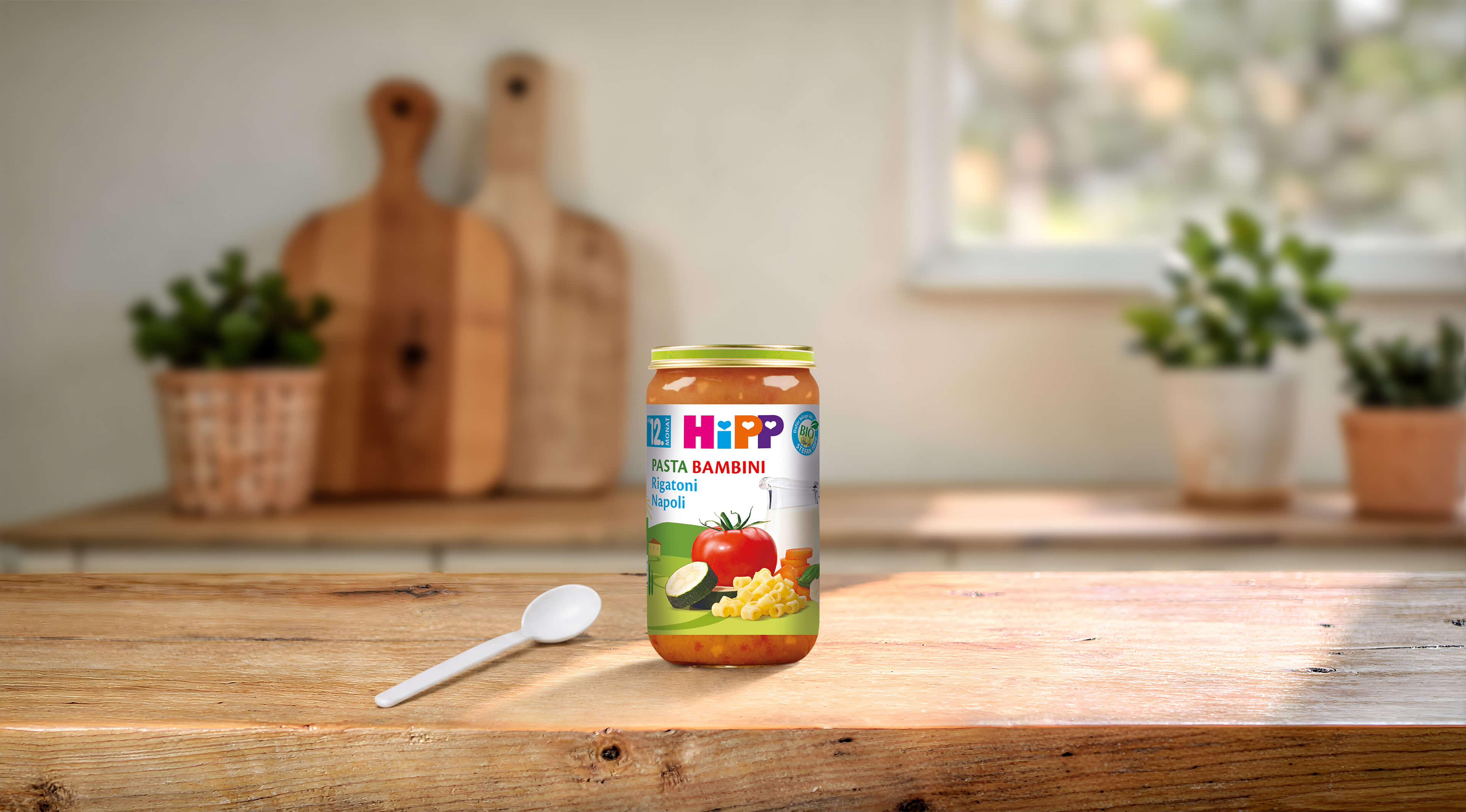 HiPP Pasta Bambini Rigatoni Napoli Bio-Glas auf Holztisch mit Löffel in heller, gemütlicher Küche