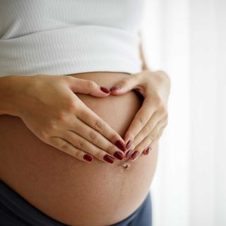 Die Hände einer Person bilden eine Herzform über dem schwangeren Bauch.